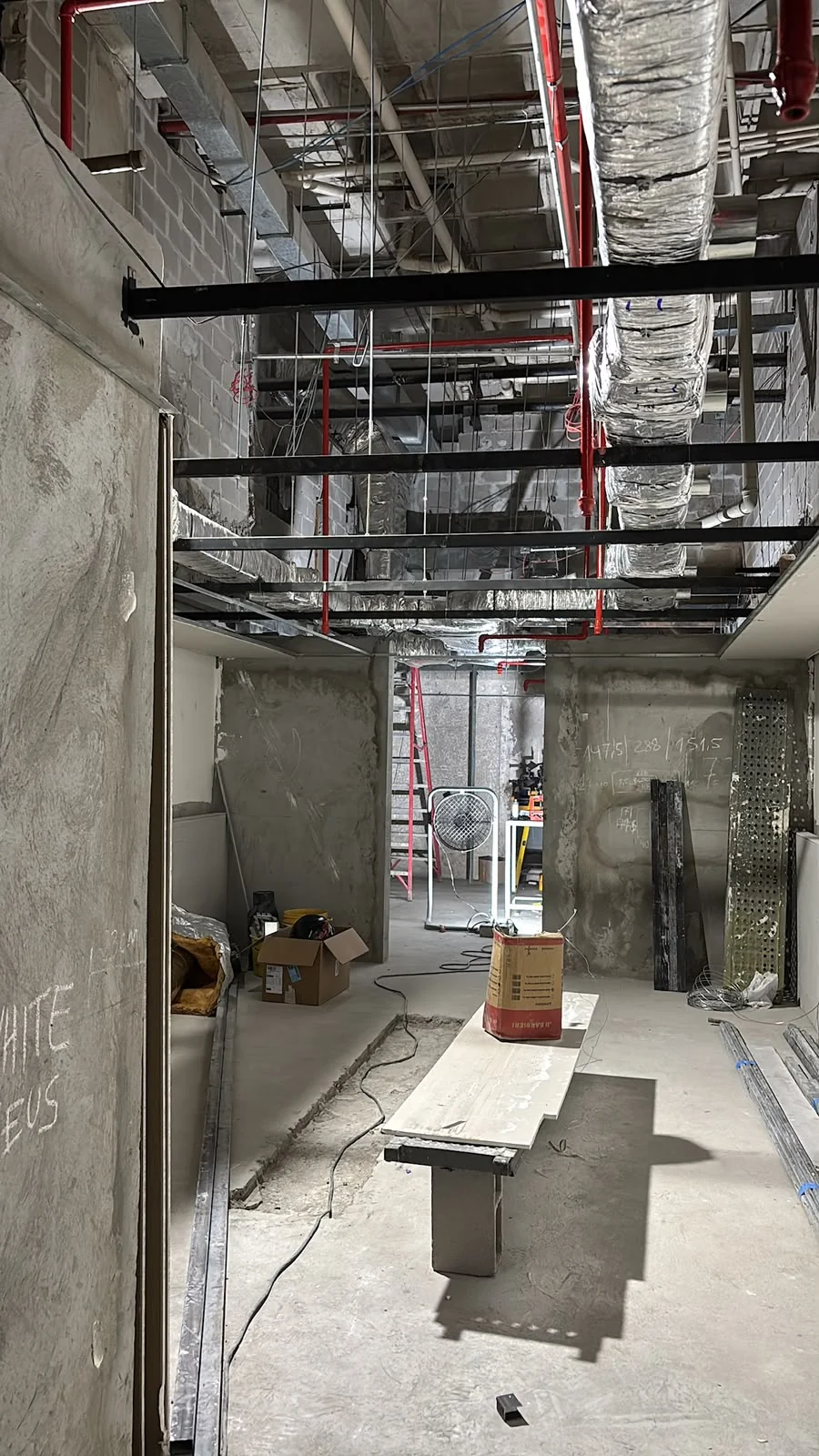Ambiente interno em obra com dutos, tubulações e suportes metálicos aparentes no teto.